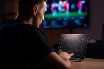 SLO16 Games — Discover modern slots and table adventures A man celebrating a winning moment on his laptop while gaming symbols float around him, capturing the excitement of SLO16 games.